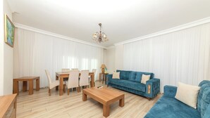 A living room with a blue sofa, wooden coffee table, and a dining area with chairs and a table. - FAMILY HOME (İstanbul)