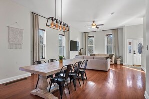 Un vaste espace de vie comprenant une table à manger en bois, des chaises noires, un canapé et un ventilateur de plafond.