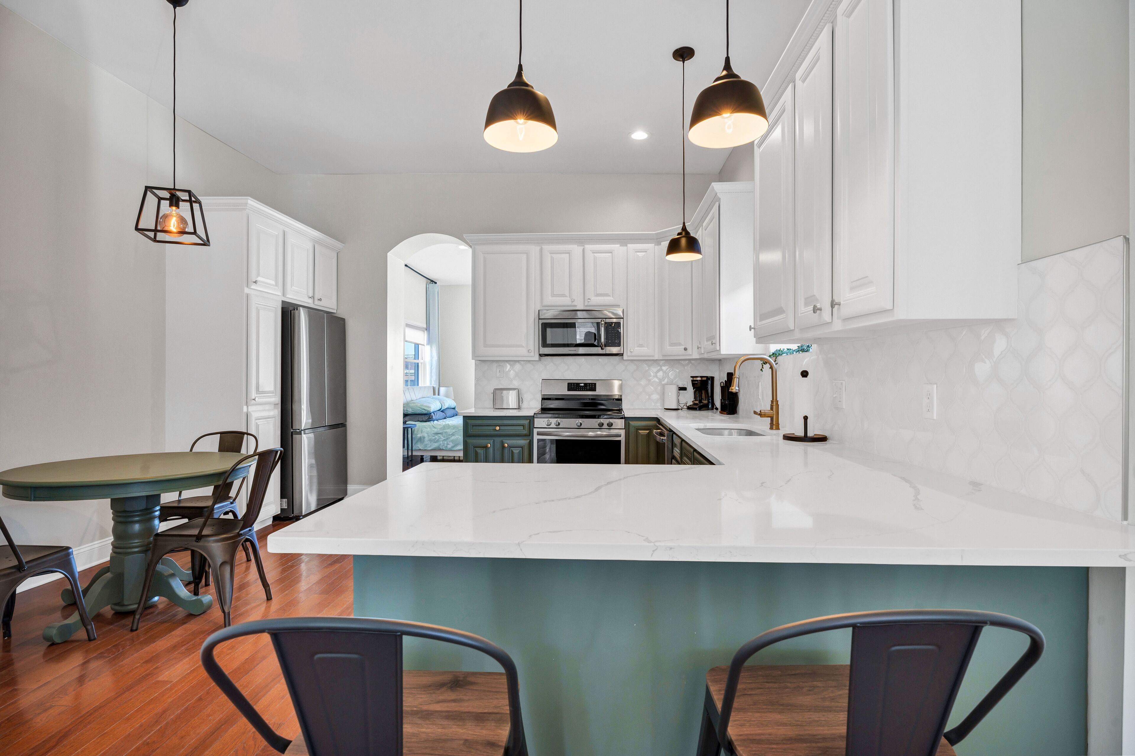 A modern kitchen with white cabinets, a large island, stainless steel appliances, and pendant lighting.