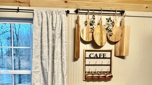 A rustic kitchen with a wooden table and two stools, a hanging pot rack, and a window with a view of trees. - Cozy CABIN on a PRIVATE LAKE in Cabot, AR (Cabot)