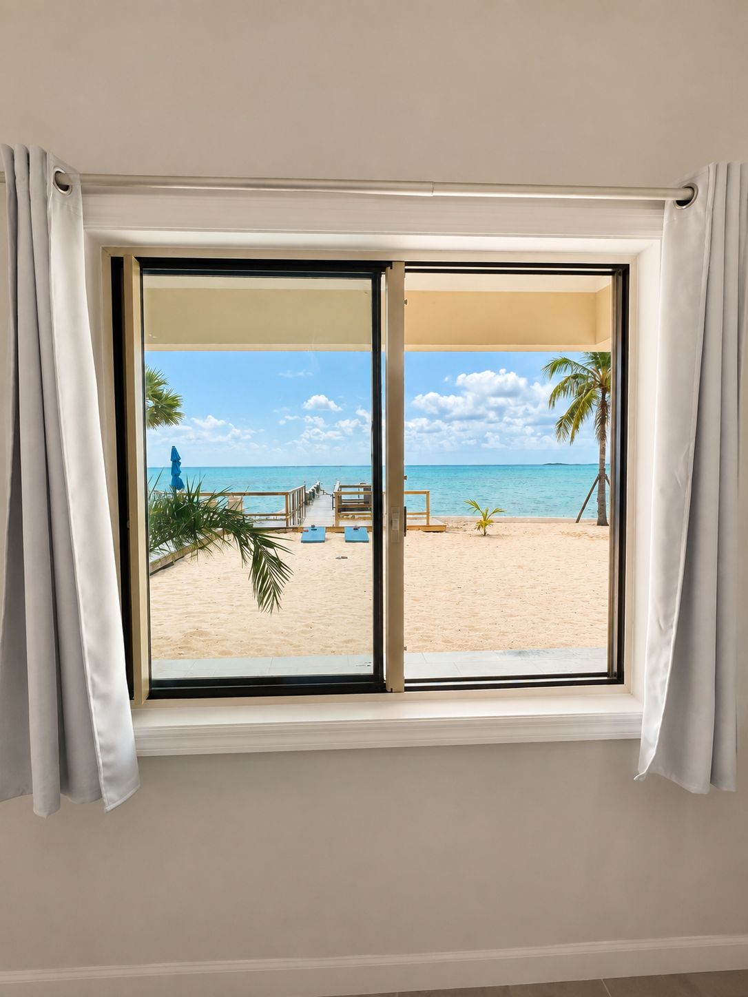A window with a view of a beach, including a sandy area and palm trees.