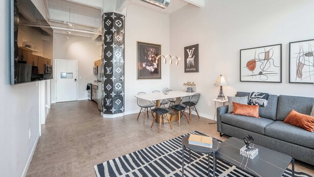 A modern living room with a grey sofa, a black coffee table, and a dining area with a white table and chairs. - The 333 Suites 301 - Suite for 6 (Cincinnati)