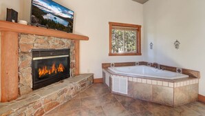 A bathroom with a stone fireplace, a large bathtub, and a window. - Knotty by Nature - Hot Tub, Pets & Fun - Oh my! (South Lake Tahoe)