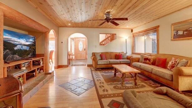 A cozy living room with a wooden ceiling, a television, a sofa set, and a large window. - Knotty by Nature - Hot Tub, Pets & Fun - Oh my! (South Lake Tahoe)