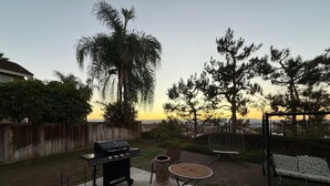 En udendørs terrasse med grill, siddepladser og solnedgangsudsigt.
