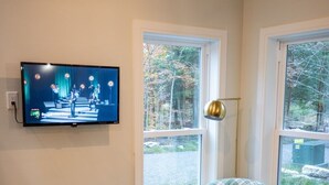 Una sala de estar con un televisor montado en la pared, un sillón amarillo junto a una ventana, y un sofá verde con cojines amarillos.