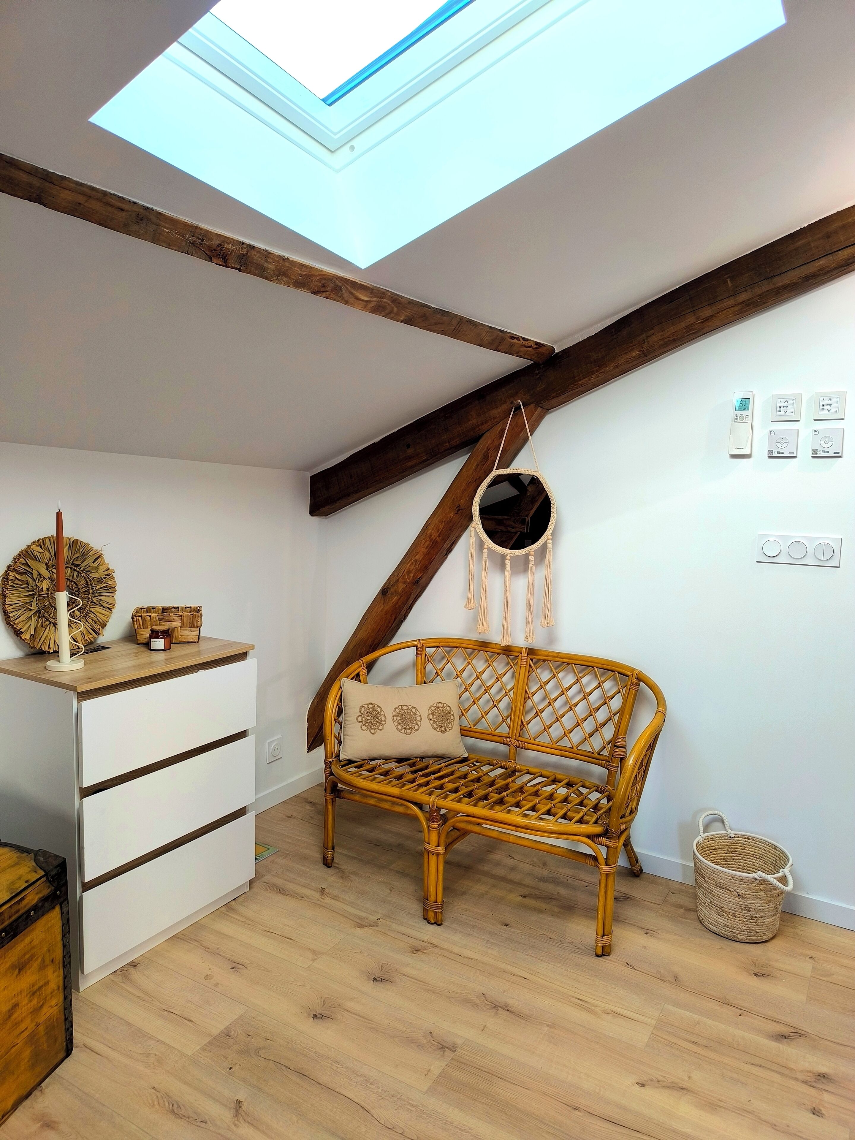 Una habitación con techo inclinado, un banco de madera, un aparador blanco y un tragaluz.