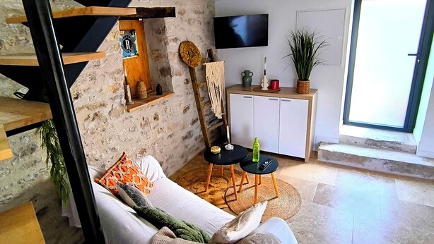 A modern living space with a stone wall, a wooden staircase, a sofa, a dining table with chairs, a television, and a large window. - Casa Liã Guest House (Septfonds)