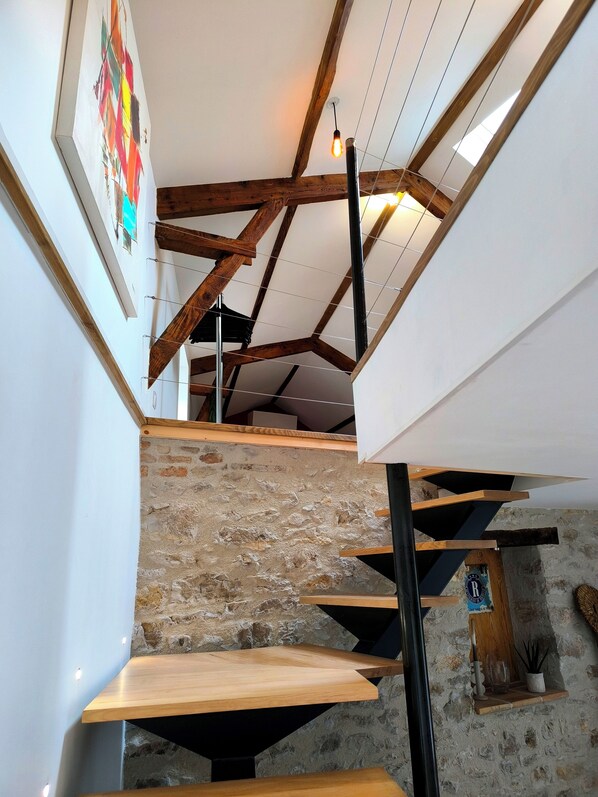 A staircase with wooden steps and a stone wall, leading to a room with a wooden ceiling and a framed picture on the wall. - Casa Liã Guest House (Septfonds)