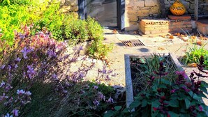 A stone building with a black door, surrounded by a garden with various plants and flowers. - Casa Liã Guest House (Septfonds)