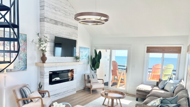 A modern living room with a fireplace, a dining area, and a view of the ocean. - Oceanfront Penthouse with Pool & Stunning Beach Views in Murrells Inlet (Murrells Inlet)