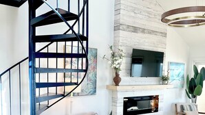 A modern living room with a spiral staircase, a fireplace, and a flat-screen TV mounted on a white wall. - Oceanfront Penthouse with Pool & Stunning Beach Views in Murrells Inlet (Murrells Inlet)