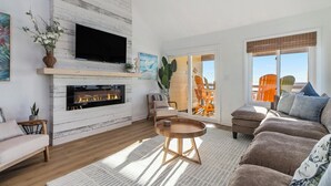 A living room with a fireplace, a sofa, a coffee table, and a TV mounted on the wall. - Oceanfront Penthouse with Pool & Stunning Beach Views in Murrells Inlet (Murrells Inlet)
