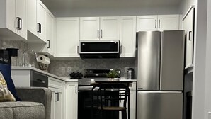 A modern kitchen with white cabinets, stainless steel appliances, and a grey sofa.