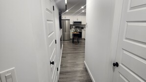 Un couloir aux portes blanches et au plancher en bois mène à une cuisine équipée.