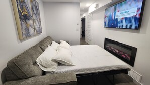 Une chambre à coucher moderne avec un lit, un canapé, un téléviseur fixé au mur et un tableau.