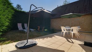 Un espace patio avec une table ronde et des chaises, un porte-parapluie en métal et un mur en pierre.