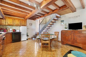 Eine Küche mit Holzausstattung, einem Esstisch mit Stühlen, einer Treppe und einem Fernseher auf einem Holzschrank.