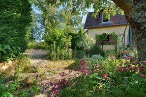 Ein Steinhäuschen mit Garten, einer Holzbank und einem Baum.