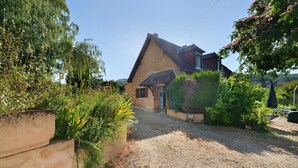Une maison avec une allée en gravier, une porte en bois et un jardin où poussent différentes espèces de plantes.