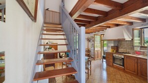 A wooden staircase leading to a kitchen with wooden beams, a dining area, and a view of the outdoors. - Holiday Home 'Écrin de Verdure' with Private Terrace, Shared Garden and Wi-Fi (Sarlat-la-Canéda)