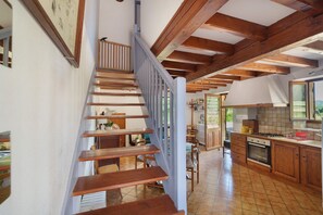Eine Holztreppe führt zu einer Küche mit Holzbalken, einem Essbereich und Blick ins Freie.