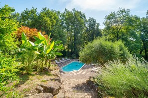 Un espace piscine agrémenté de chaises longues, entouré d’une végétation luxuriante et d’arbres.