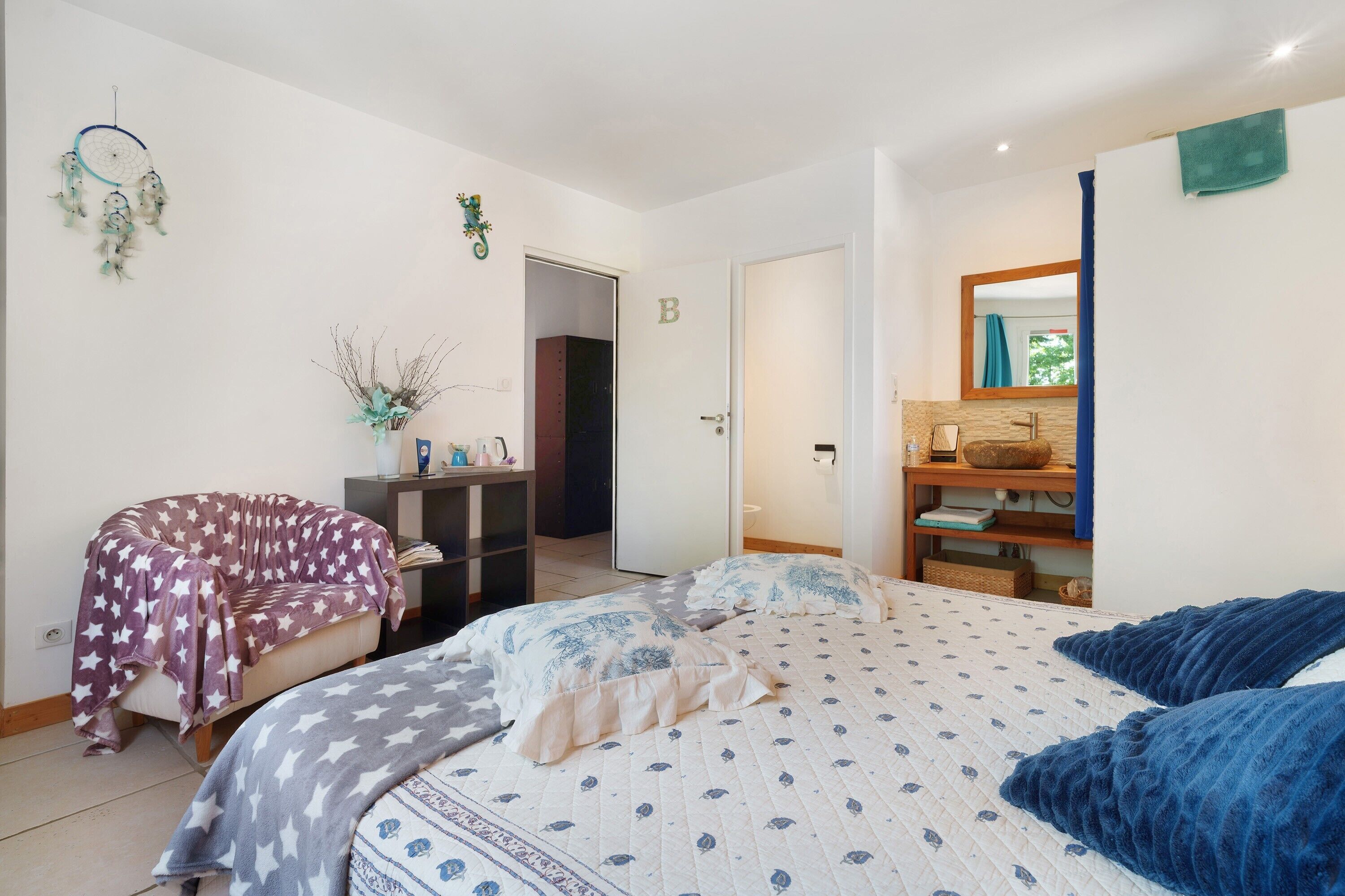 A bedroom with a bed, a chair, a desk, a mirror, and a door marked with the letter 'B'.
