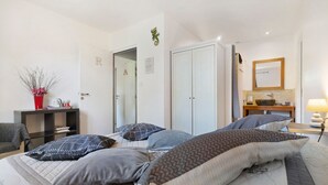 Ein Schlafzimmer mit Bett, Kissen, Nachttisch, Spiegel, Kleiderschrank und Schreibtisch mit Vase.