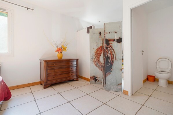 A bathroom with a toilet, a wooden dresser, and a decorative vase.