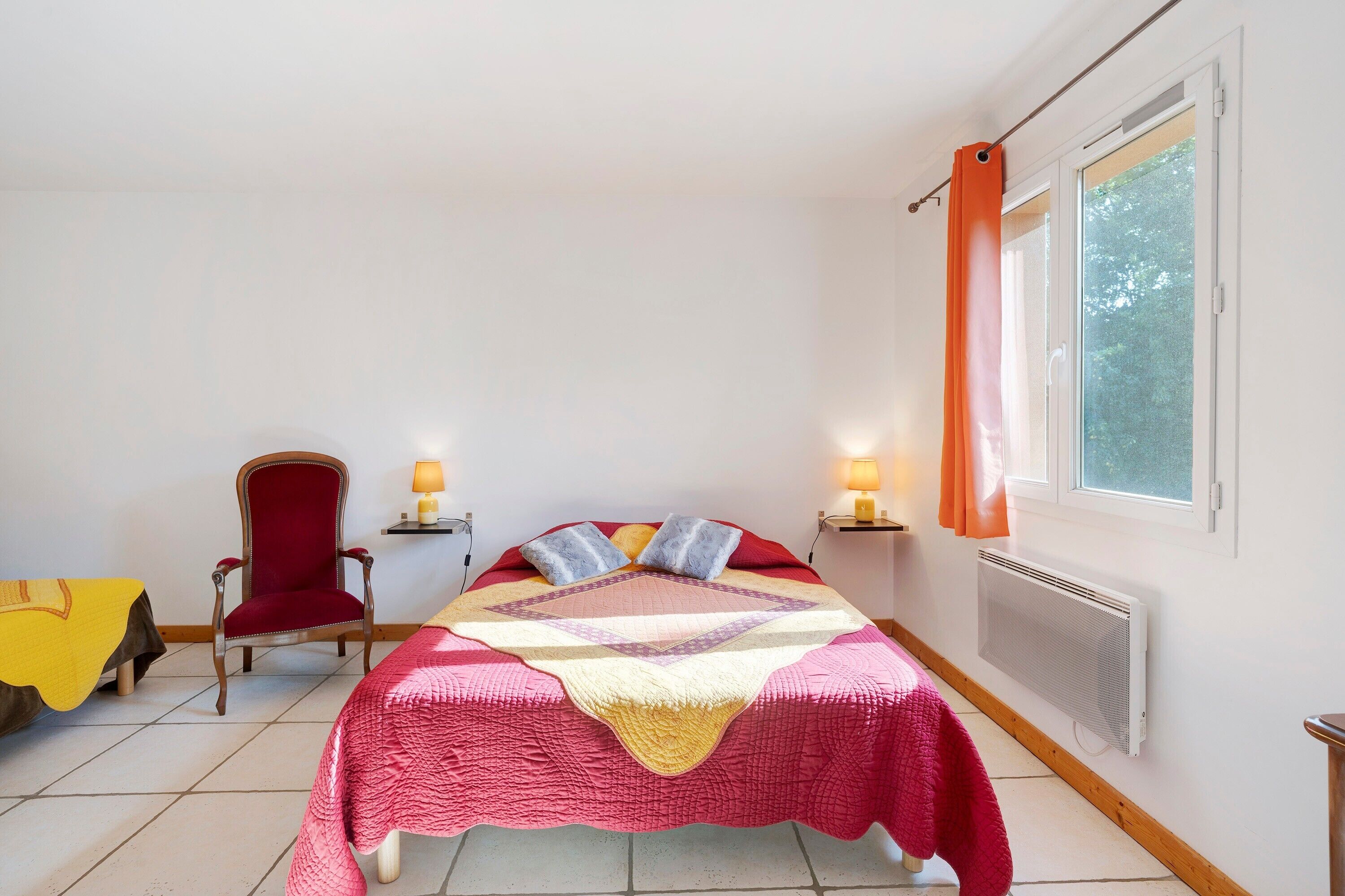 Um quarto com uma cama, uma cadeira, uma janela e um radiador.