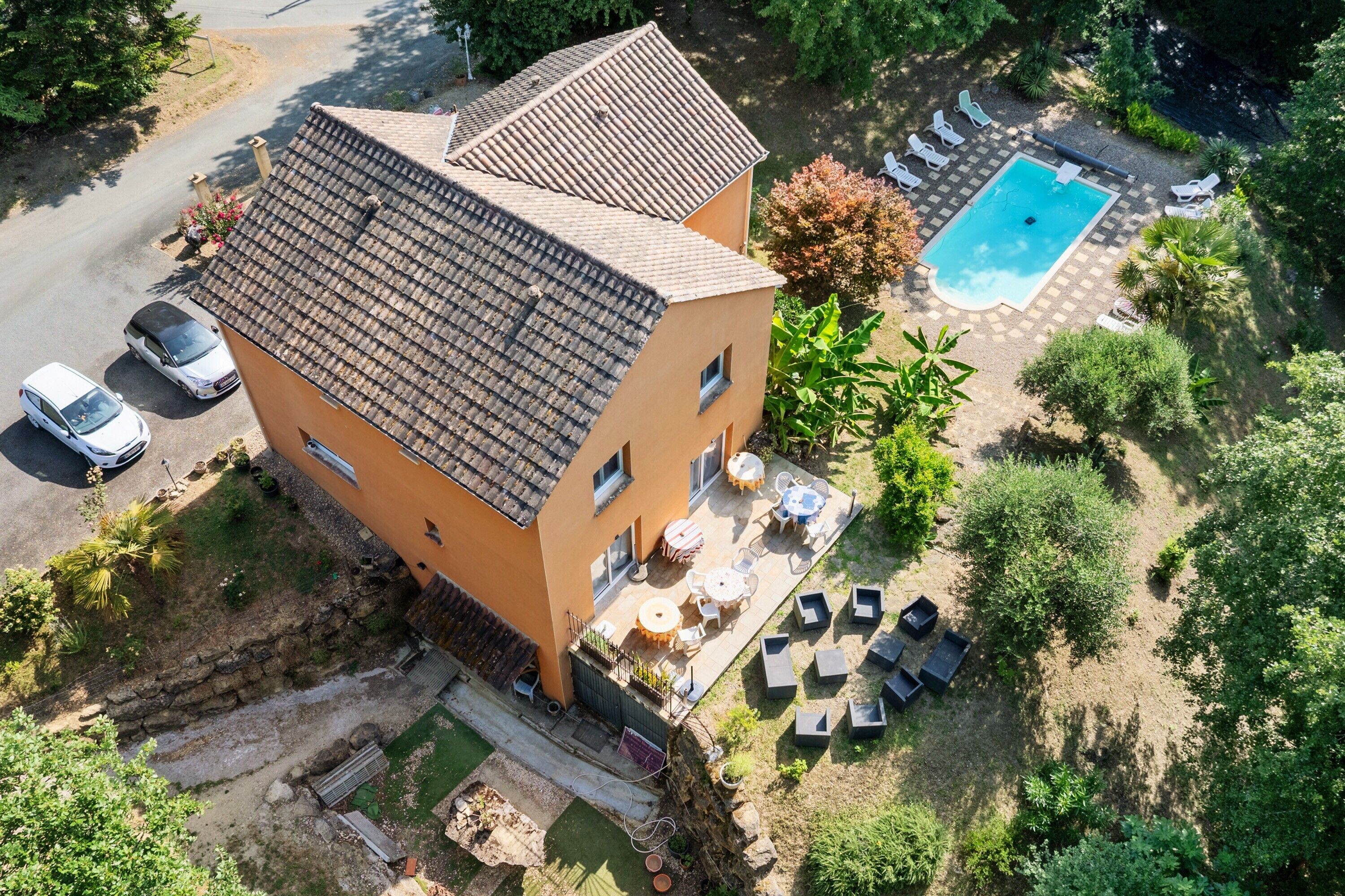 Un edificio de dos pisos con techo de tejas, piscina, mobiliario exterior y jardín.