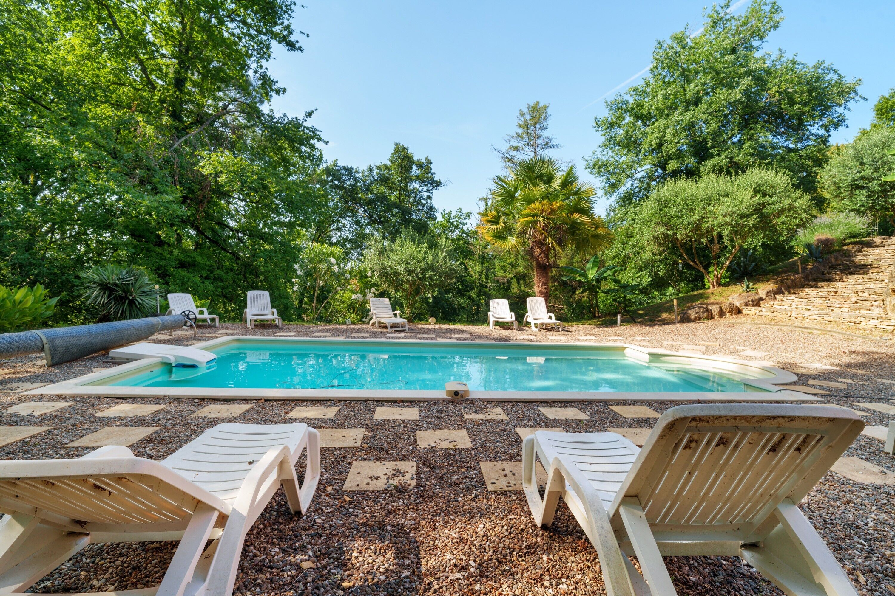 Una piscina con sillas de descanso, rodeada de árboles y un muro de piedra.