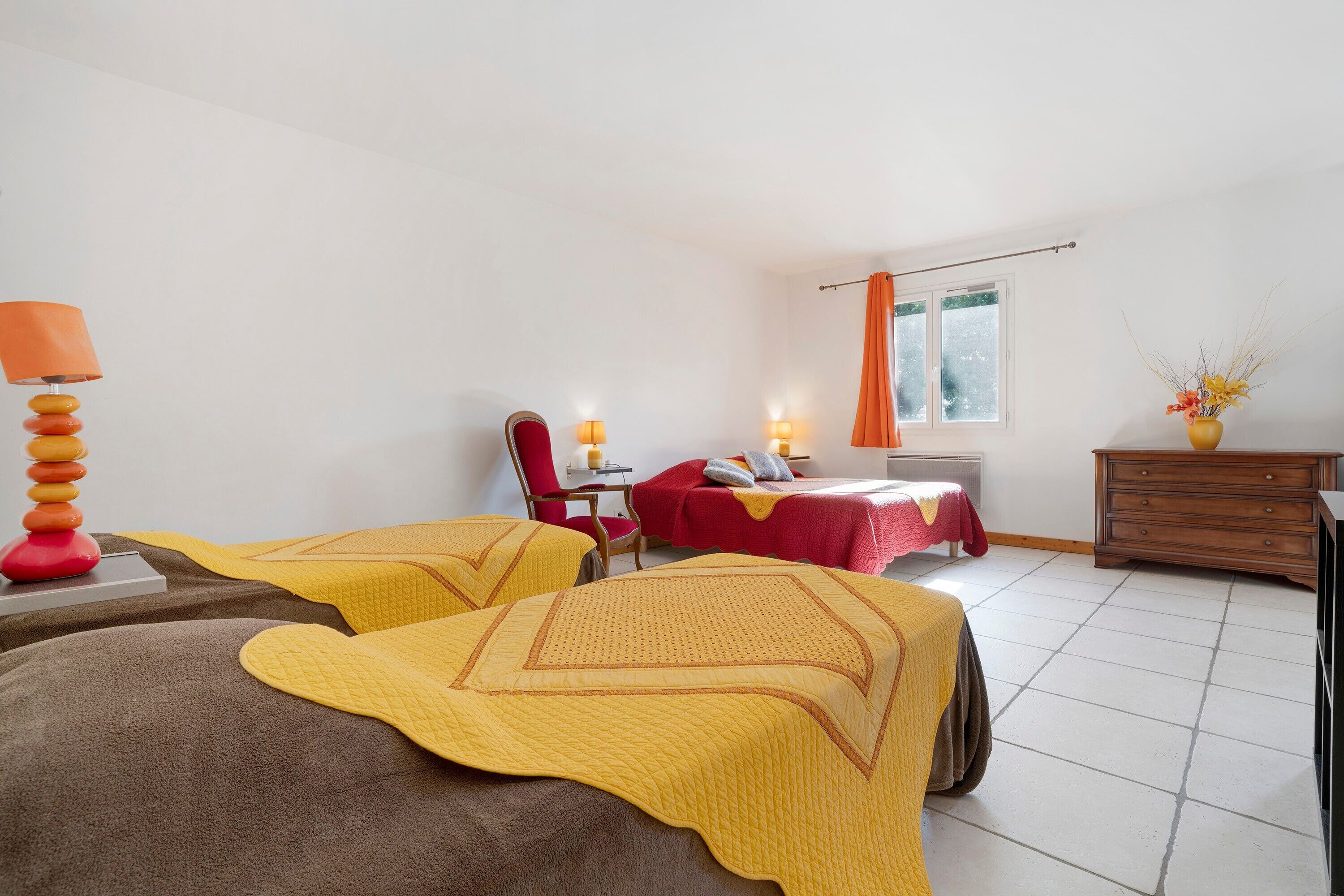 A hotel room with two beds, a desk, a chair, a lamp, a dresser, and a window.