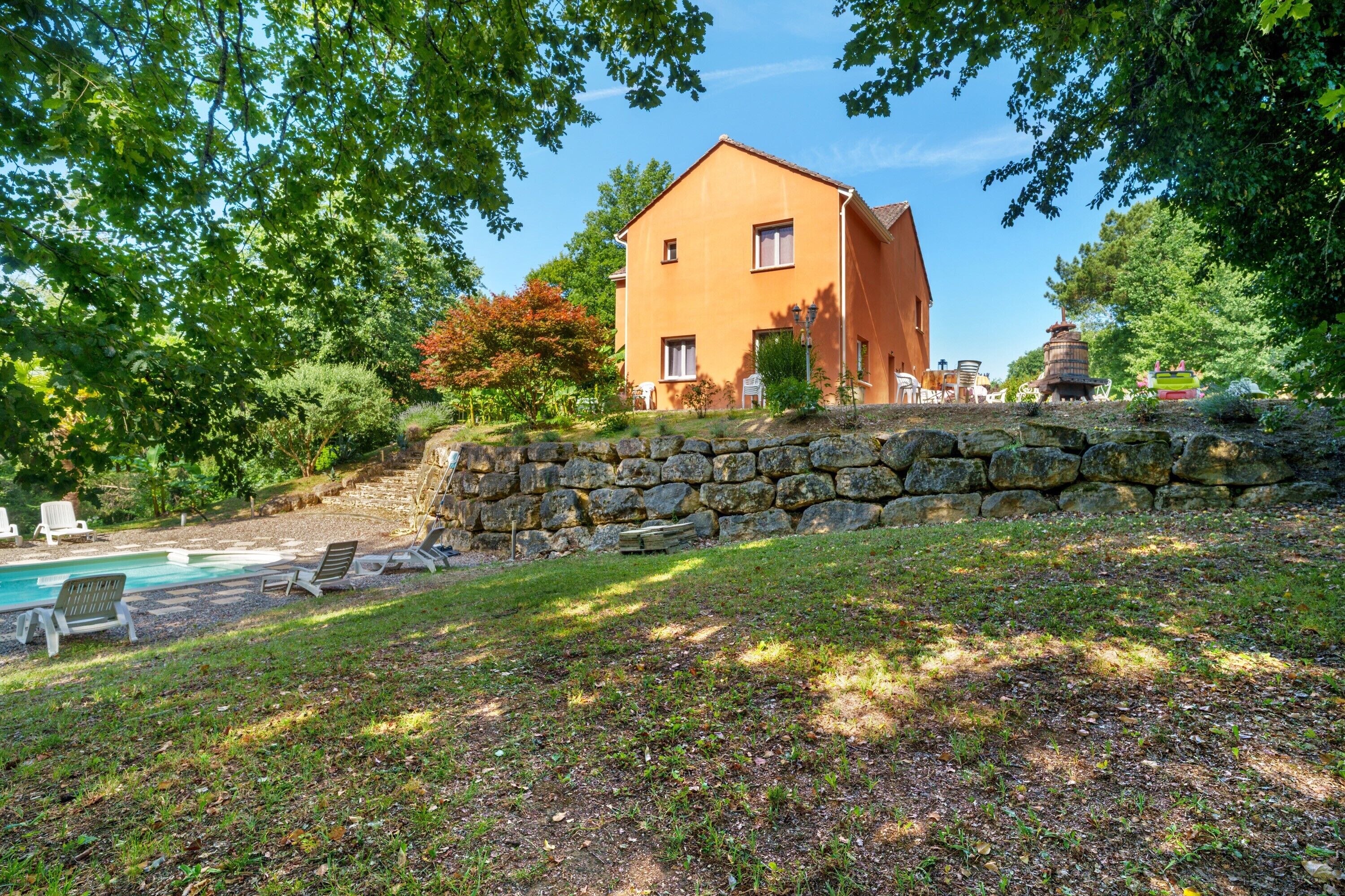 Une maison à deux étages avec un mur en pierre, une piscine et du mobilier d’extérieur.