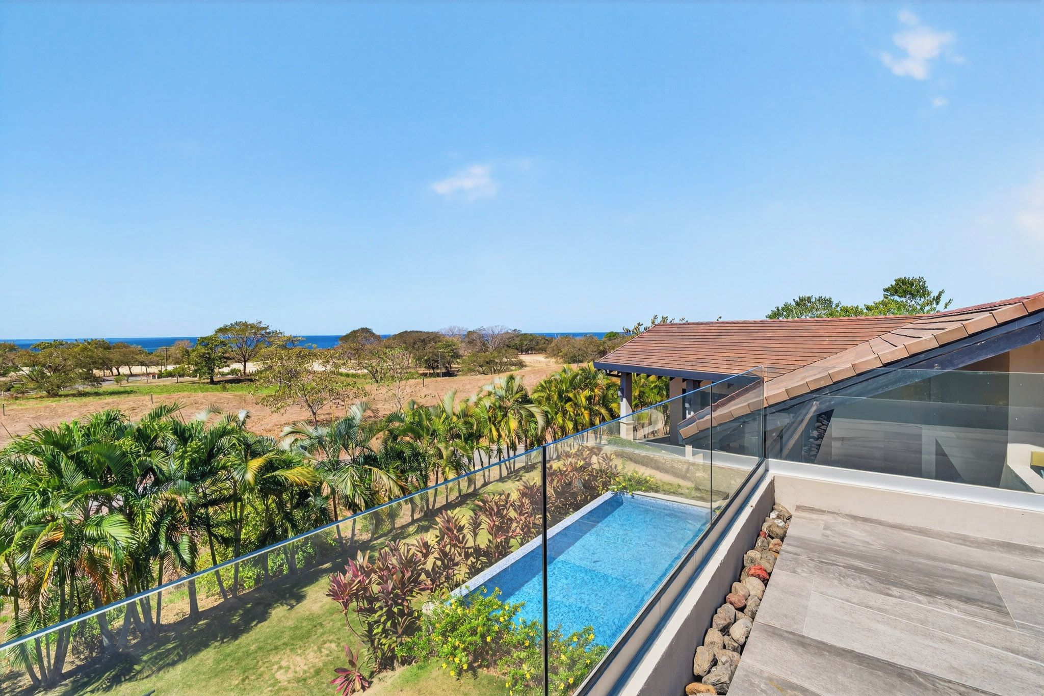 A residential property with a swimming pool, a view of the ocean, and a clear sky.