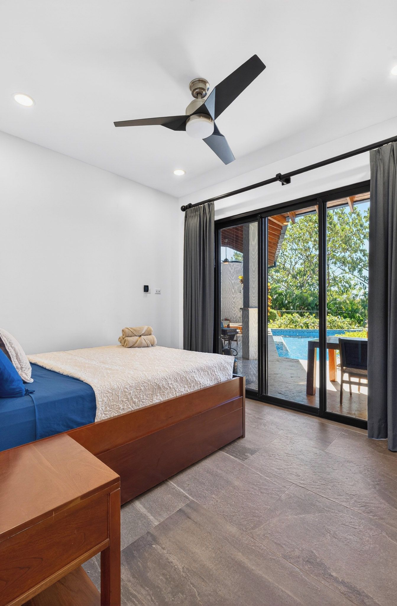 Ein Schlafzimmer mit einem Bett, einem Deckenventilator und Blick auf ein Außenbecken durch eine Schiebetür.