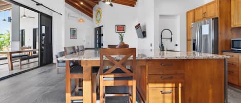 A modern kitchen with a wooden ceiling, a large island with a marble countertop, and built-in appliances.