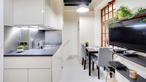 Una cocina moderna con electrodomésticos de acero inoxidable, un comedor con televisor y una planta en el alféizar de la ventana.