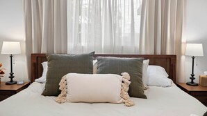 A neatly made bed with a wooden headboard, two bedside tables with lamps, and a window with sheer curtains. - Hot Tub/Pool/Fire Pit/10 Mins to Beach (San Diego)