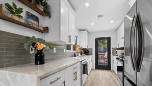A modern kitchen with white cabinets, a stainless steel refrigerator, and a tiled backsplash. - Hot Tub/Pool/Fire Pit/10 Mins to Beach (San Diego)