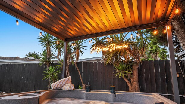 A hot tub area with a wooden pergola, palm trees, and a neon sign reading "California Dreamin'". - Hot Tub/Pool/Fire Pit/10 Mins to Beach (San Diego)