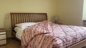 Een eenpersoonsbed met een gestreept sprei, een houten hoofdbord, een nachtkastje met een lamp en een nachttafeltje met een lamp.
