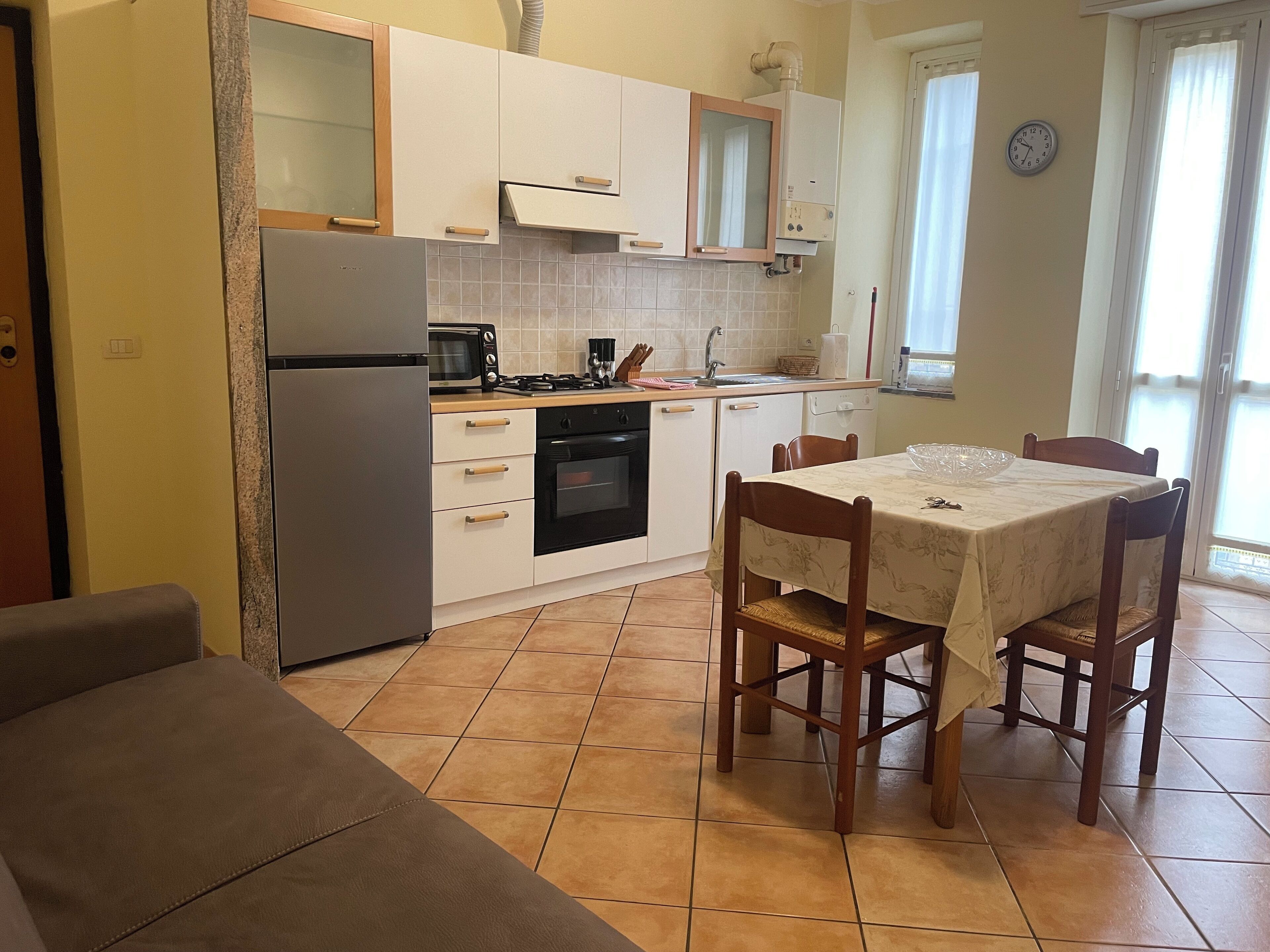 Cuina compacta amb nevera, fogó, microones i forn. Hi ha un menjador amb cadires i un sofà en primer pla.