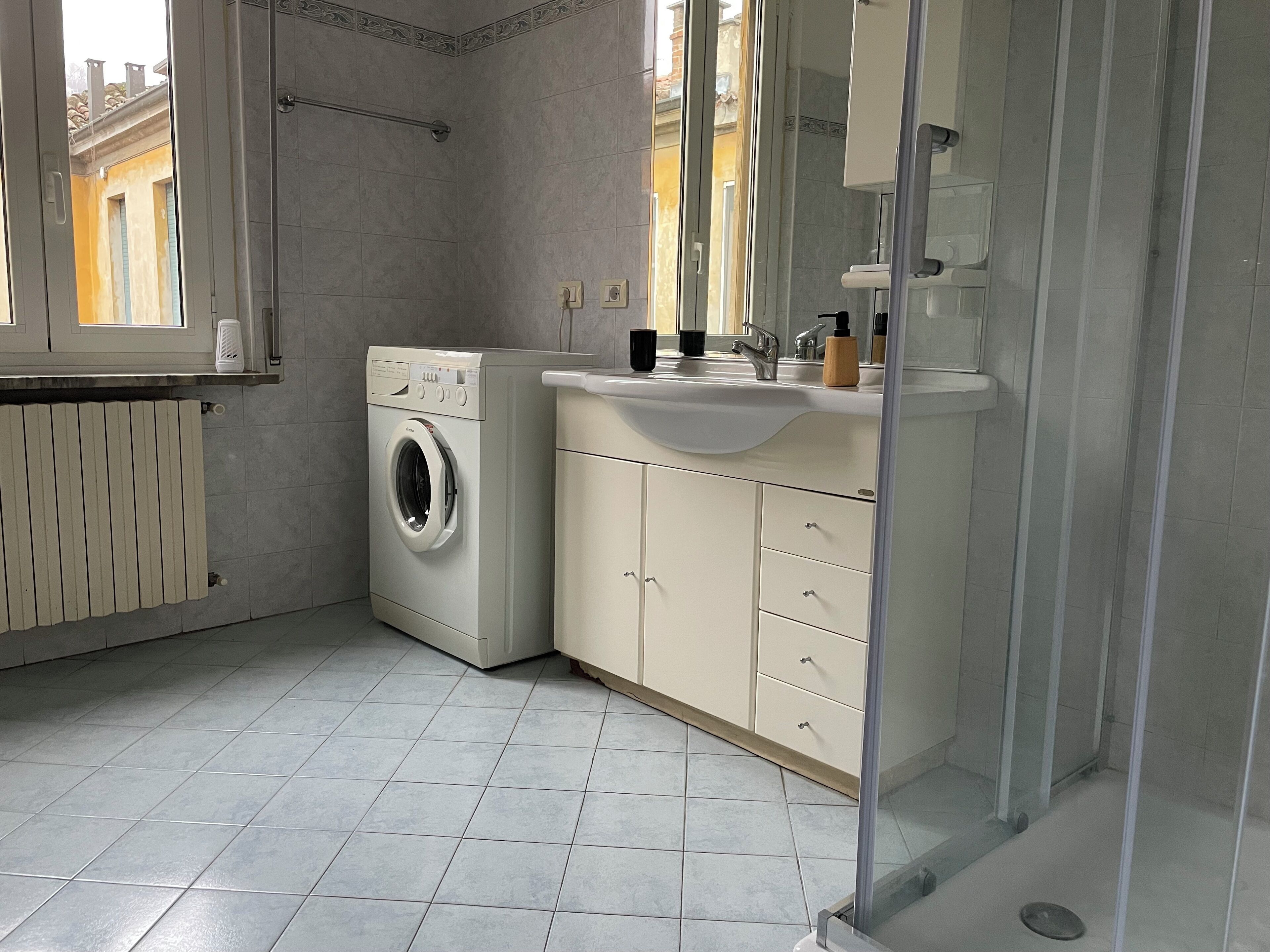 Un baño moderno con lavadora, lavamanos y cabina de ducha de vidrio.