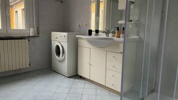 Un baño moderno con lavadora, lavamanos y cabina de ducha de vidrio.