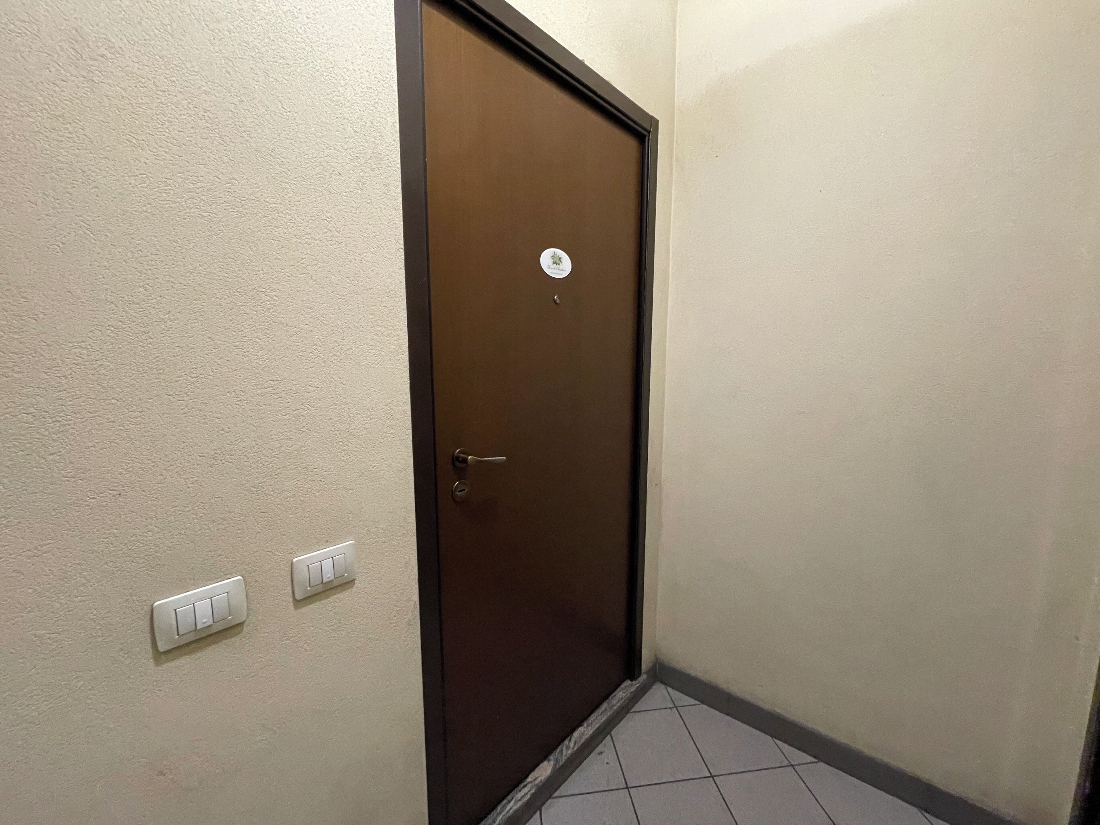 Una puerta cerrada con un cerrojo, un interruptor de luz y una pequeña pegatina en la pared.
