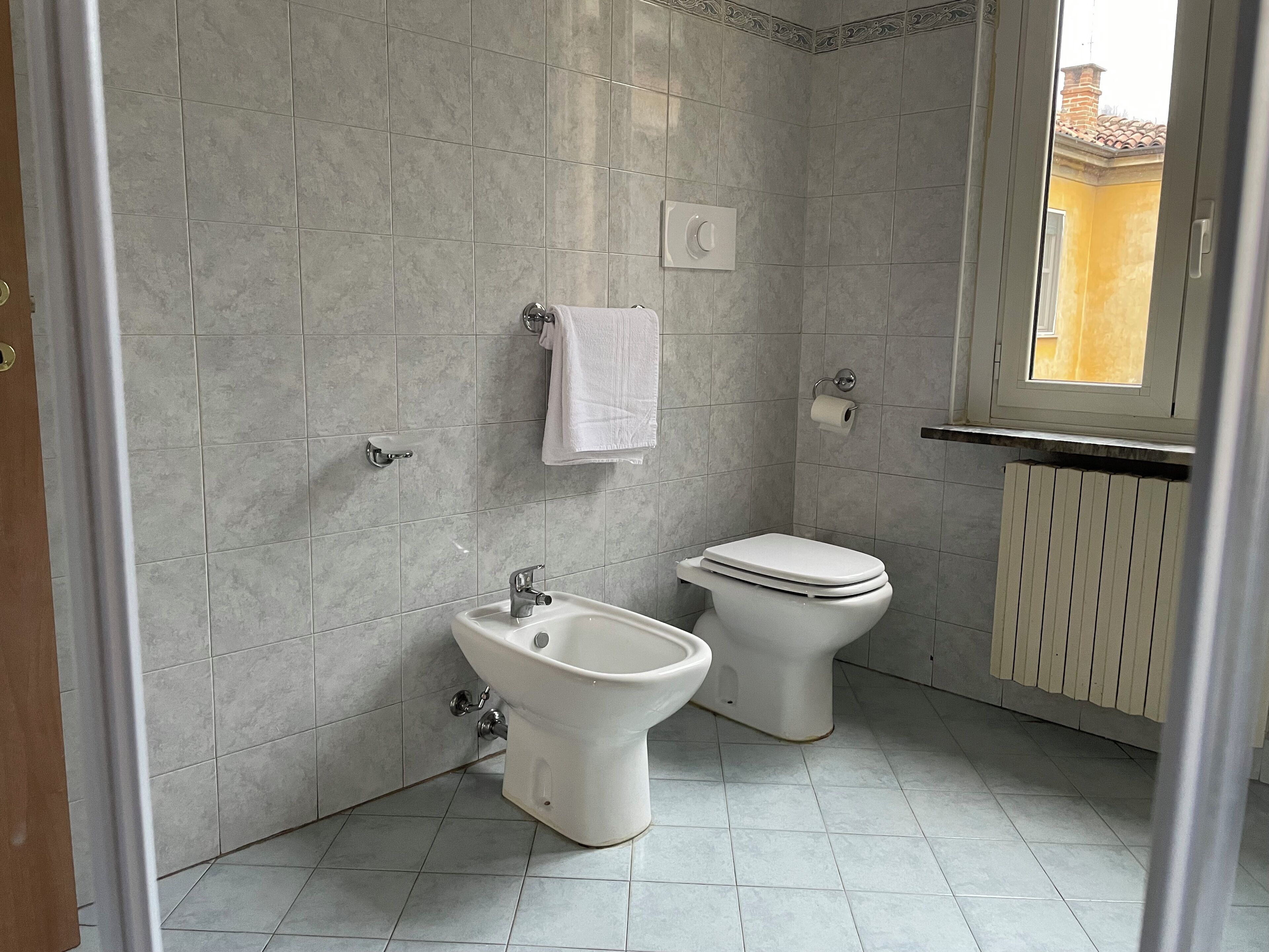 Un bagno con bidet, servizi igienici e una finestra che offre vista su un edificio.