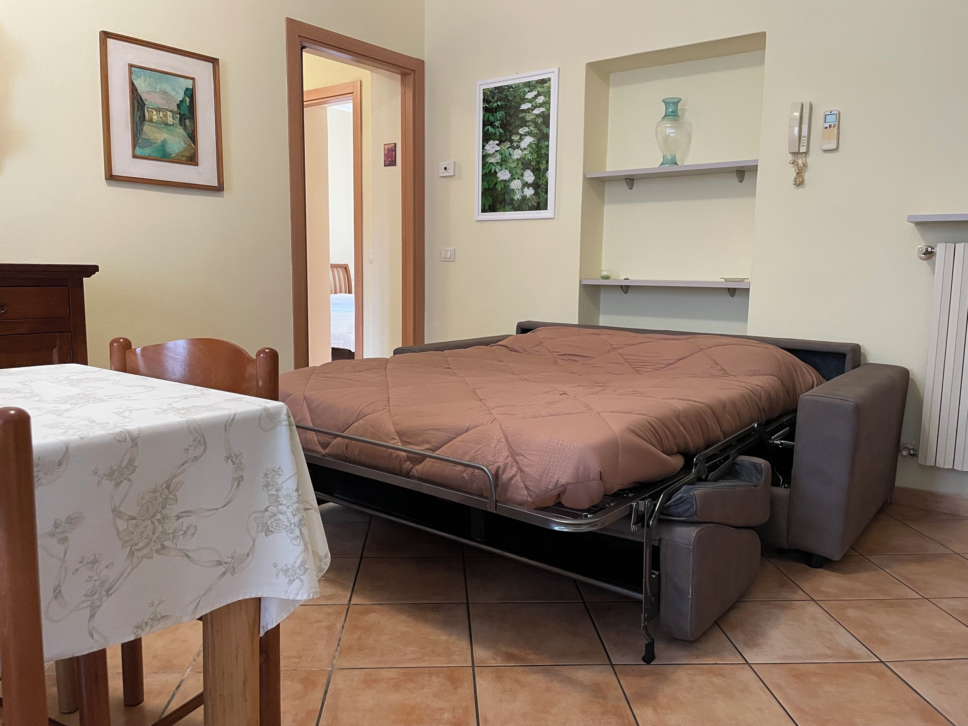 Un dormitorio con cama, una silla, una mesa y una estantería con un jarrón.