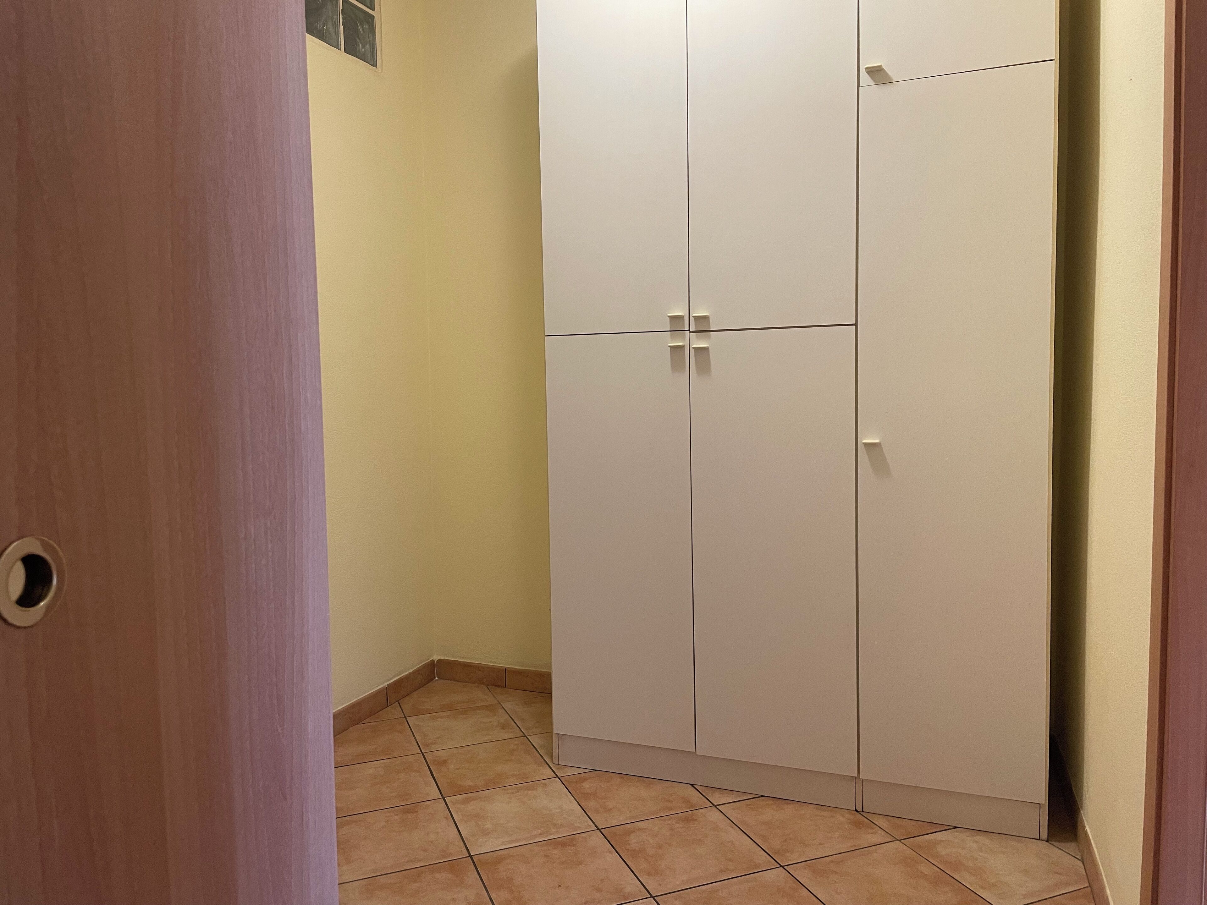 A hallway with a white wardrobe, a door with a round handle, and a tiled floor.